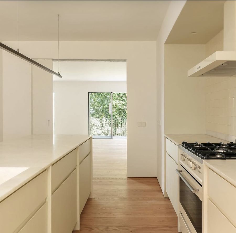 Cream galley kitchen, cream cabinets, cream stone counter, white subway tile backsplash, visible stainless gas range and white extractor hood, light oak floor, track lighting